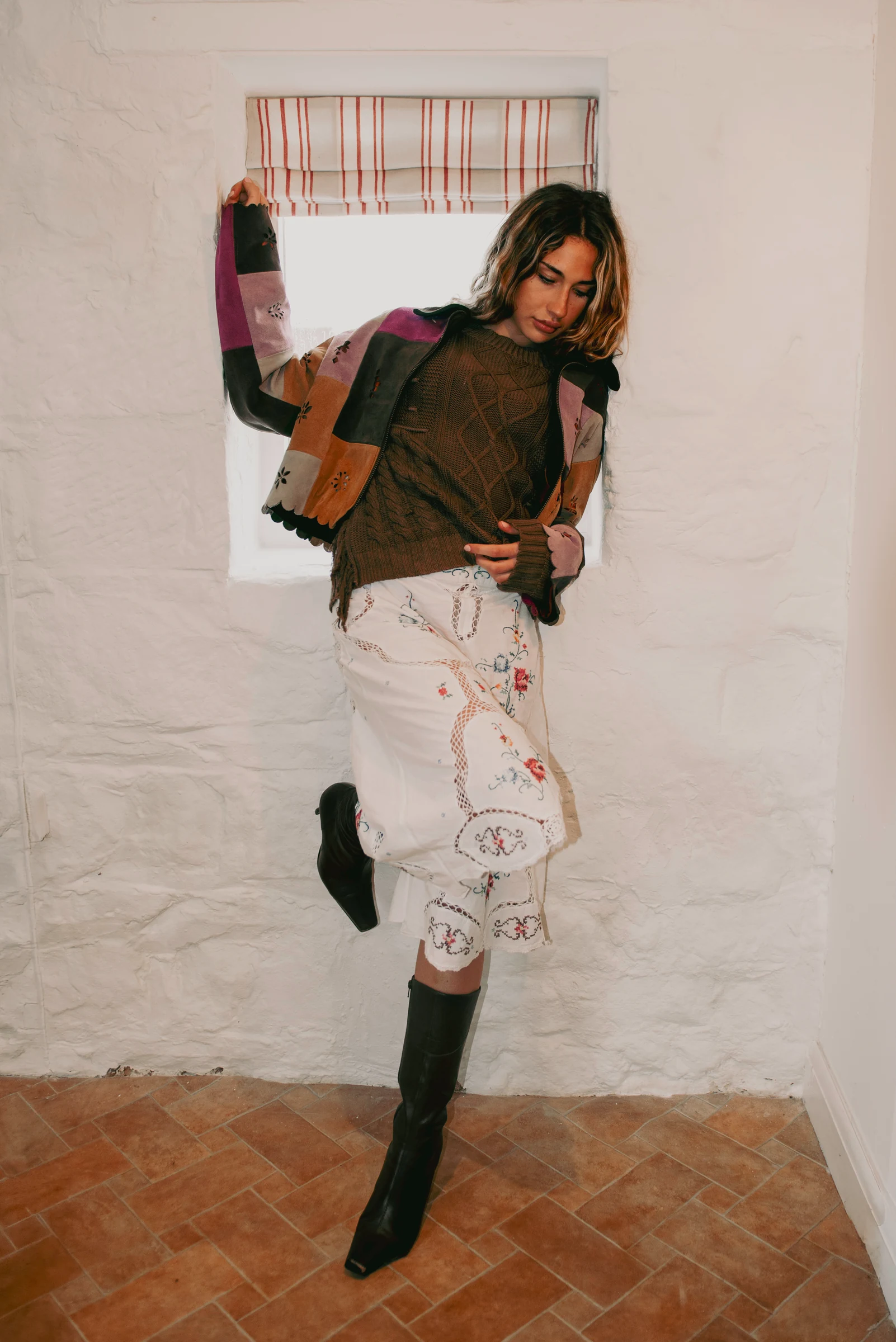 Look 1 — standing model wearing a suede patchwork jacket, brown cable knit and embroidered white skirt