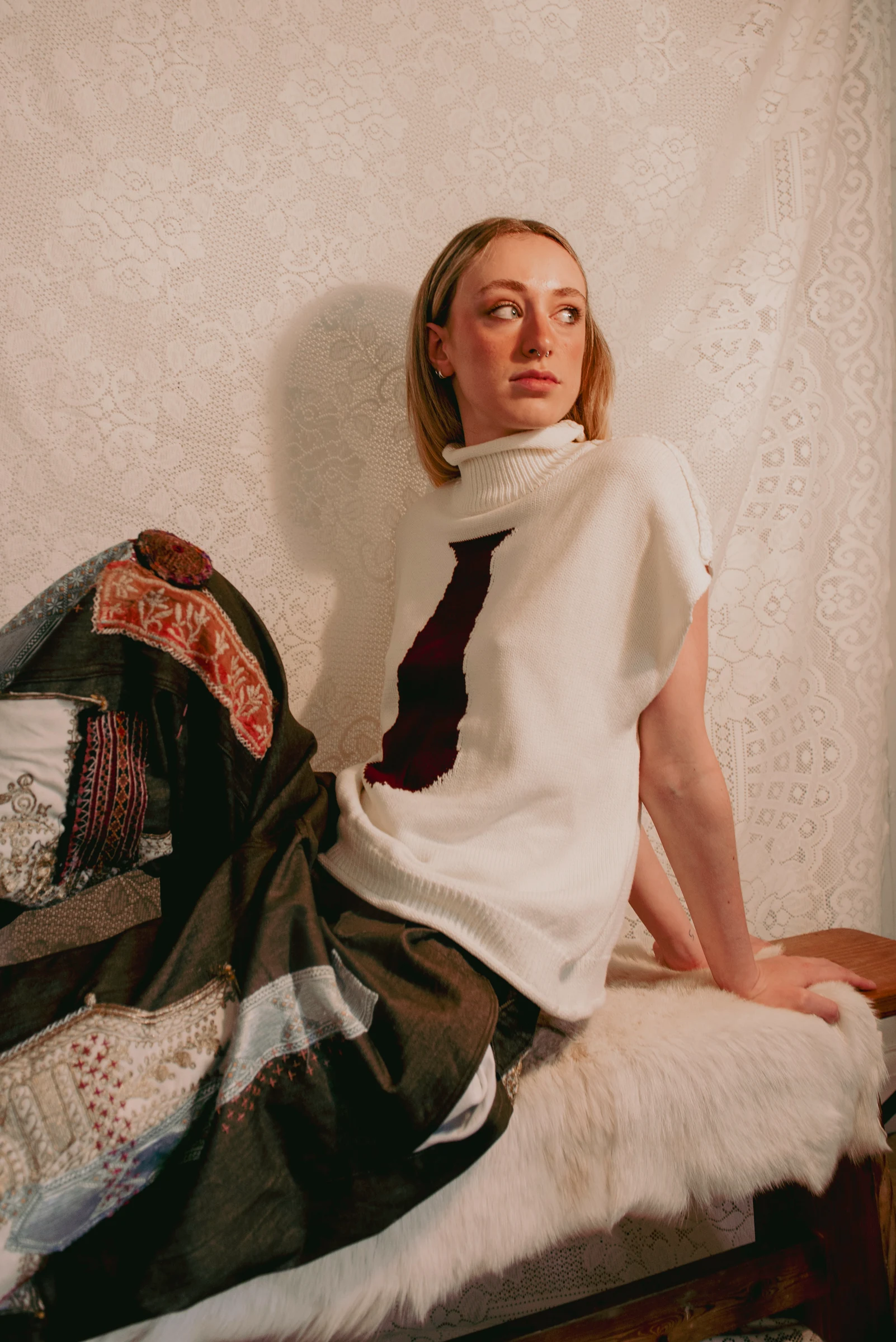 Look 4 — seated portrait showing the knitwear and layers of patterned patches on the jeans