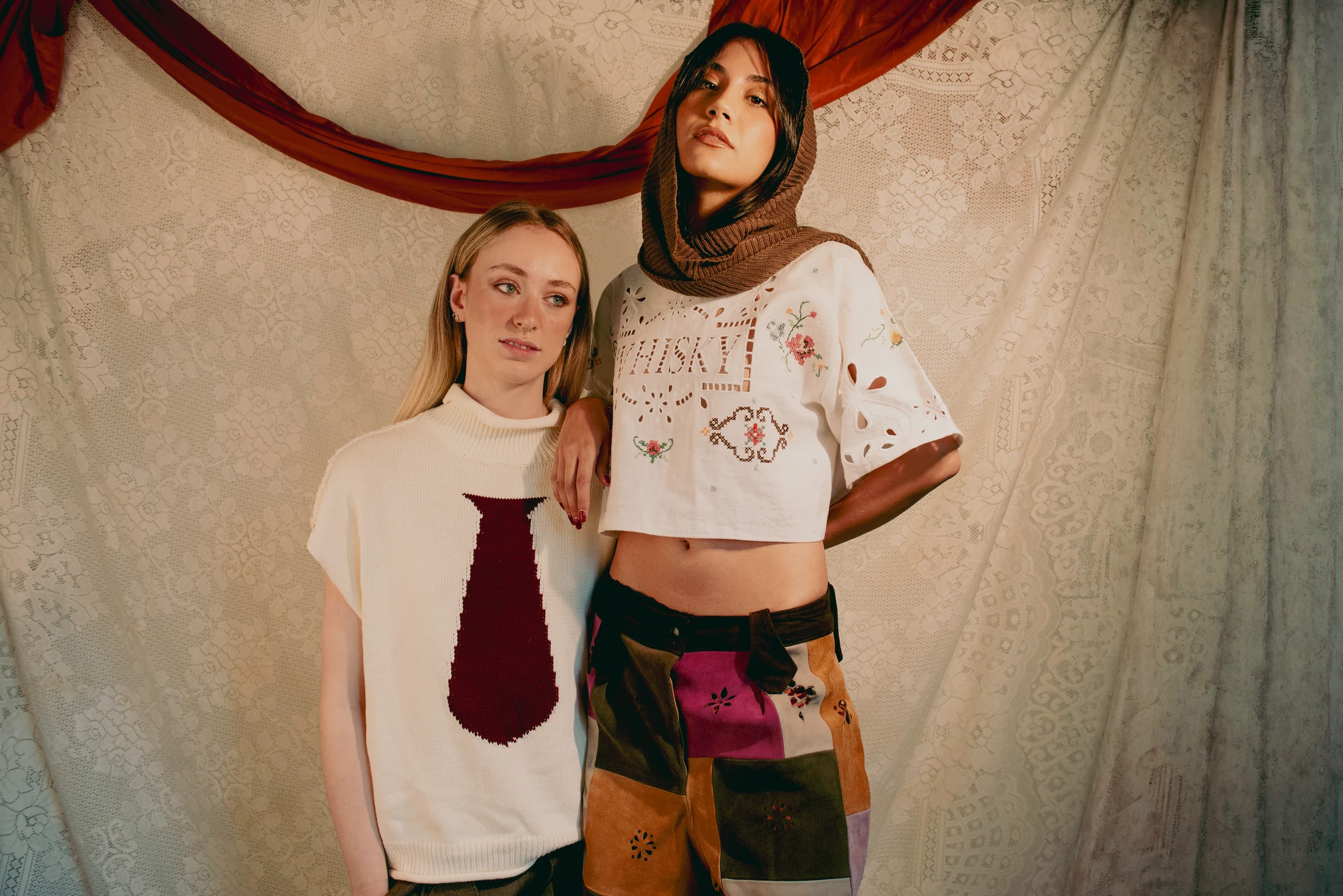Two models in the cream knit and embroidered cutwork top, styled with patchwork trousers and shorts